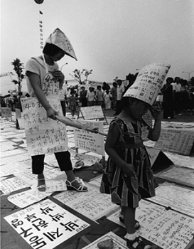 헤어진 가족의 사연을 찾는 두 모녀 자칫 이산가족을 찾는 수 많은 사람틈에서 아이를 잃을까 어머니가 우산으로 딸과 자신을 연결해 다니며, 이산가족의 사연을 읽고 있다